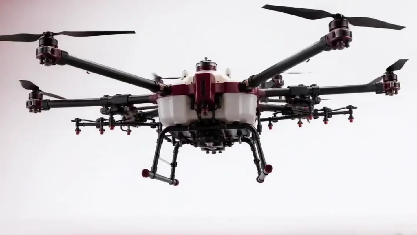 Drone de pulverização agrícola em voo, em vista lateral, com as oito hélices em movimento.